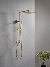 Load image into Gallery viewer, Polaris Lux rain shower set with handheld shower in brushed gold colorway appearing on a concrete grey bathroom wall with green plant on the side. Brushed gold adds glamour to a modern minimalist surrounding.
