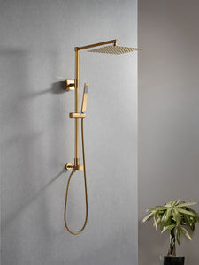 Polaris Lux rain shower set with handheld shower in brushed gold colorway appearing on a concrete grey bathroom wall with green plant on the side. Brushed gold adds glamour to a modern minimalist surrounding.